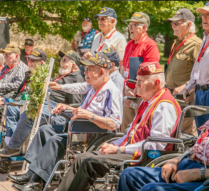 Veterans seated outdoors during a commemorative gathering.