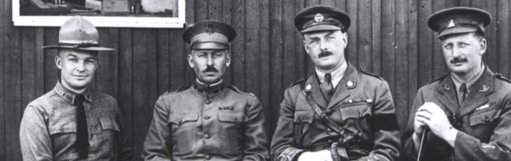 Four men in military uniforms, seated beside one another. They all appear to be from an older time period, with their attire and hairstyles indicative of a historical era.