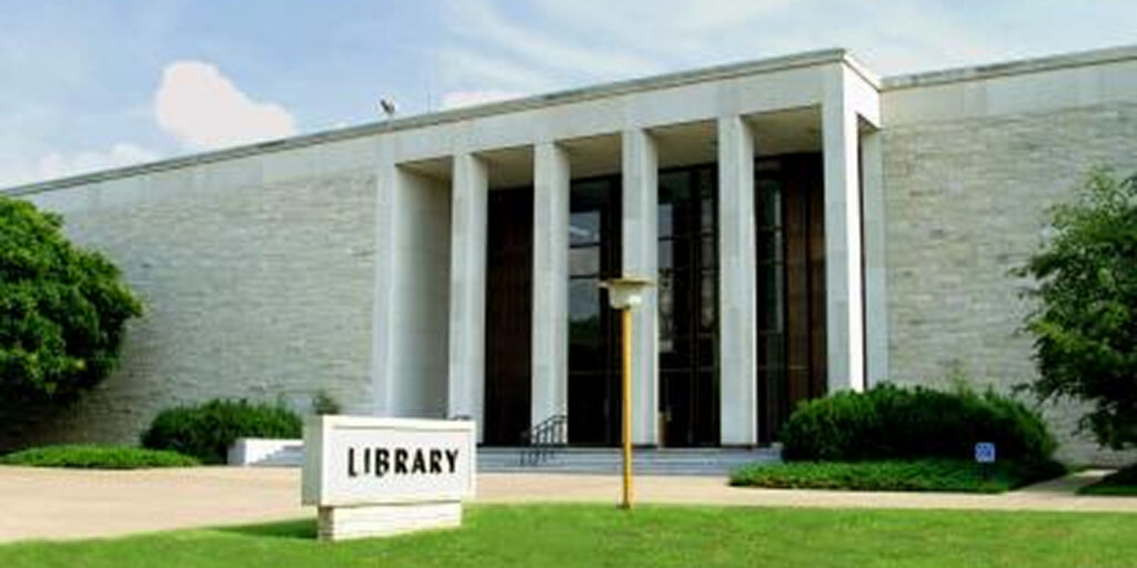 Large library building with "library" signage. The structure has multiple windows and appears to be modern with a covered walkway.