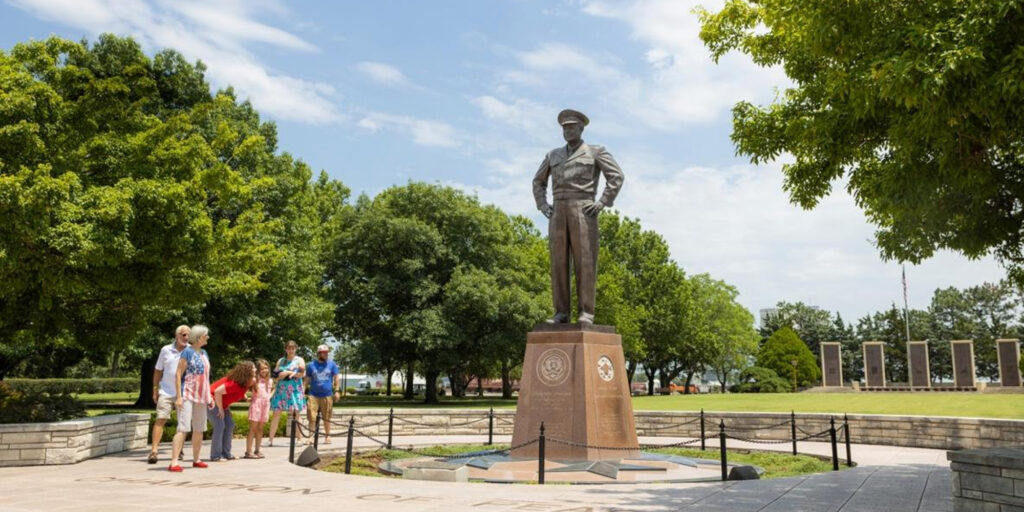 A statue of Dwight D. Eisenhower in a park, witrh people standing around base.