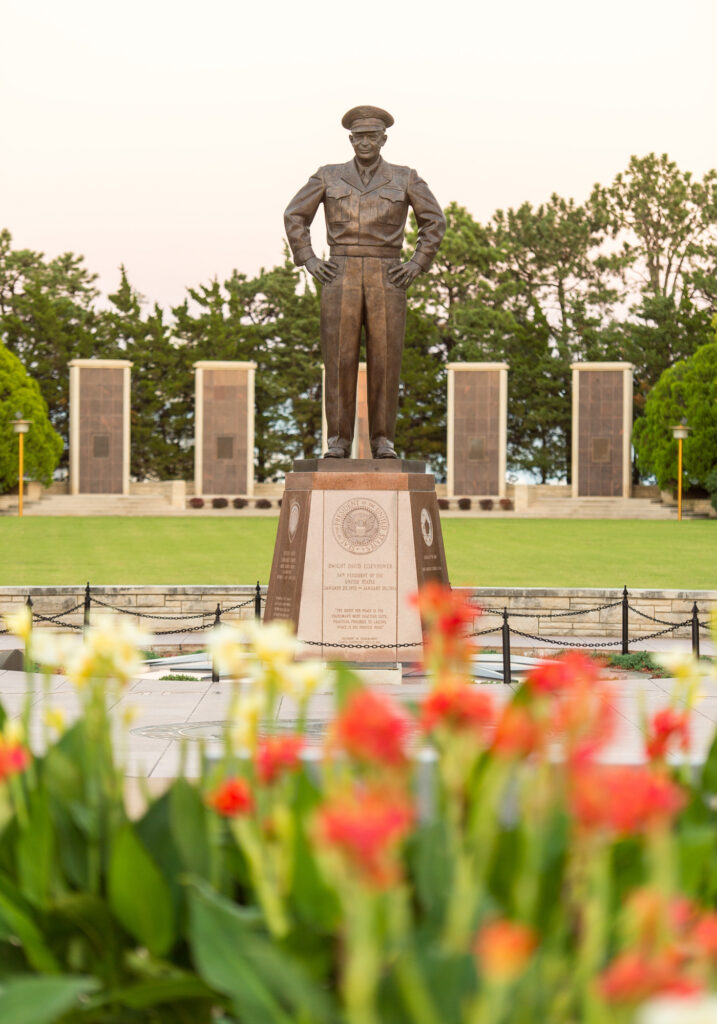A monument to Dwight D. Eisenhower, surrounded by a well-maintained garden with flowers and a blue sky background.