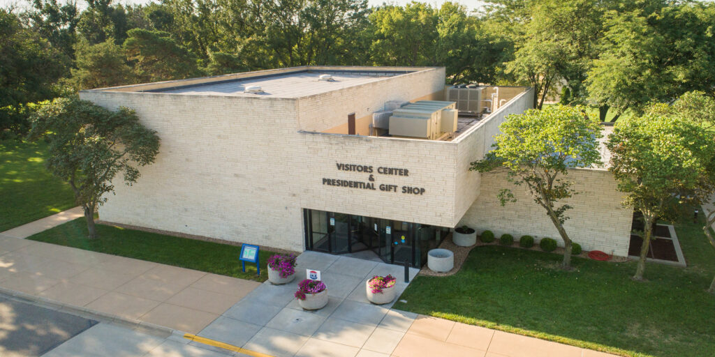 Modern building with a flat roof and large windows, featuring white walls and a sign that reads "Visitors Center & Presidential Gift Shop."