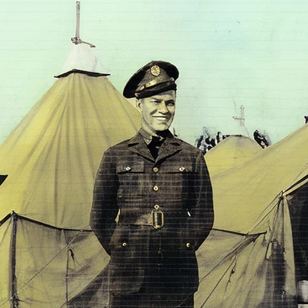 A man in military uniform posing near army tents. He is smiling while posing for the photograph.