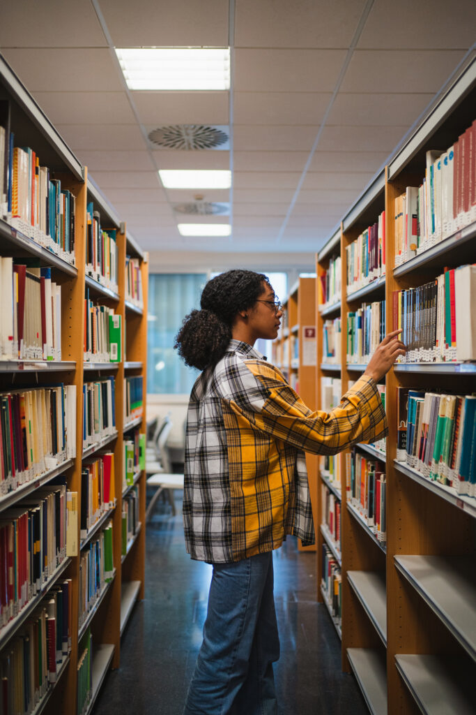 A woman in a library browsing books on a bookshelf.