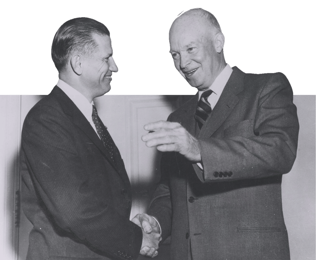 Dwight D. Eisenhower shaking hands with another man. Both are wearing suits and ties.