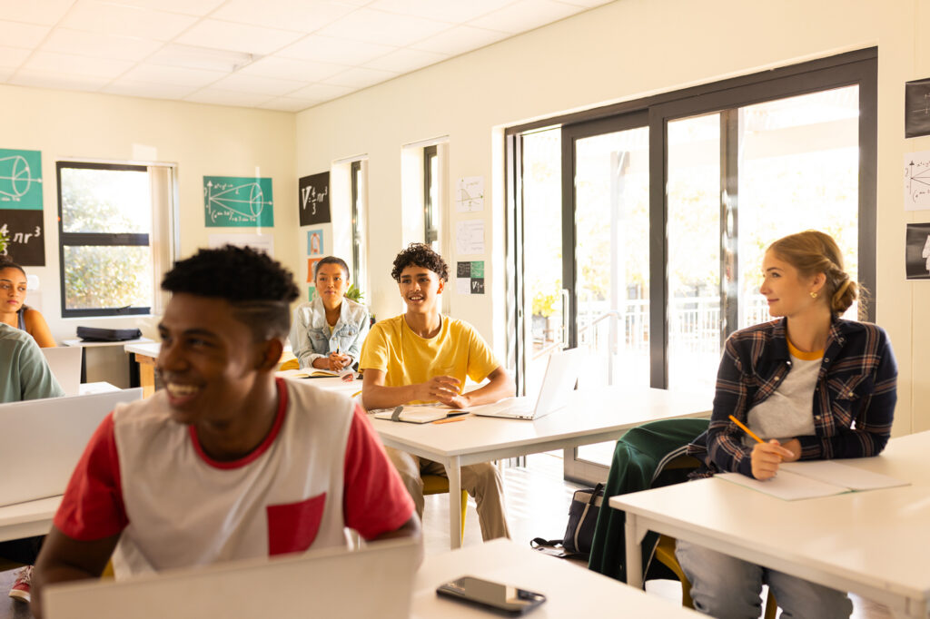 Students in a classroom, smiling and looking forward as an instructor stands by.