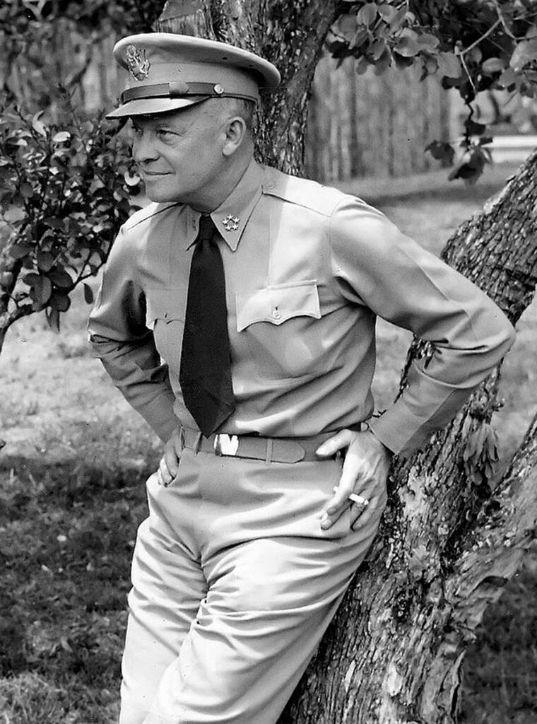 Dwight D. Eisenhower wearing a tie, leaning against a tree in a park setting.