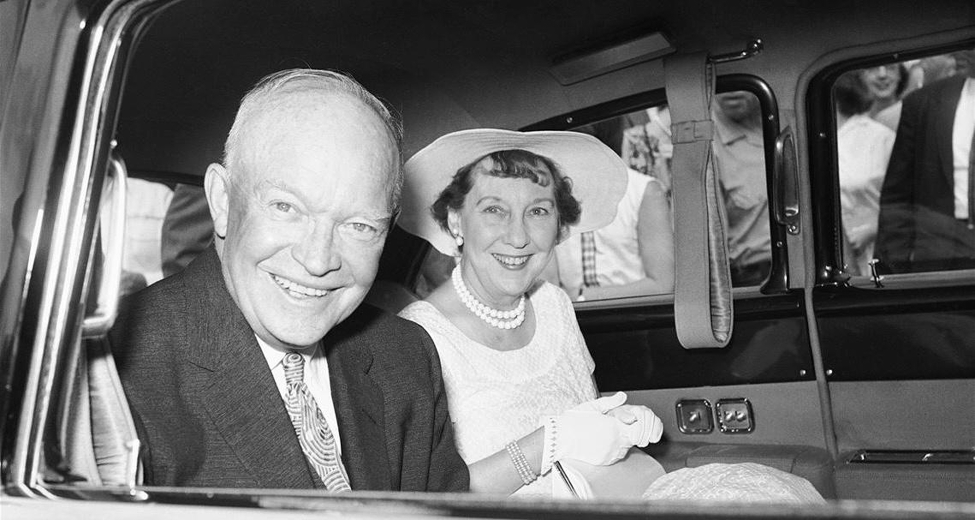 A black-and-white photograph of Dwight D. Eisenhowerand and his wife seated in a car, smiling at the camera.