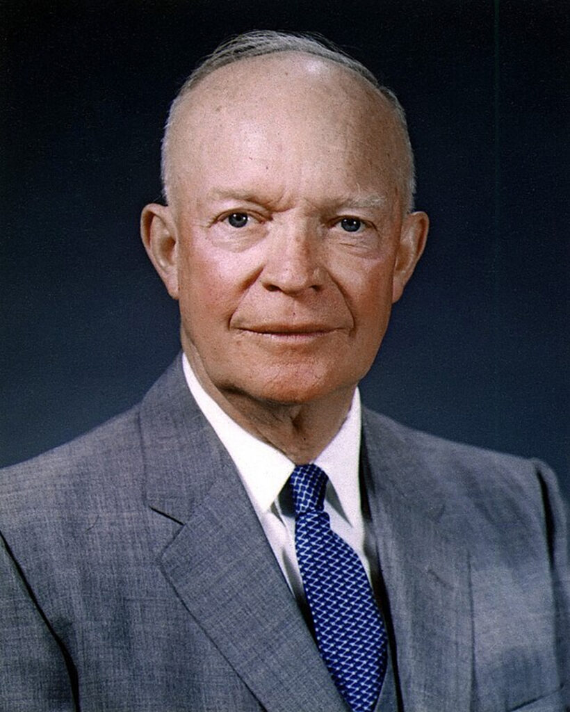 The image shows Dwight D. Eisenhower posing for a portrait photograph. He is wearing a dark suit with a light blue tie and a white shirt.