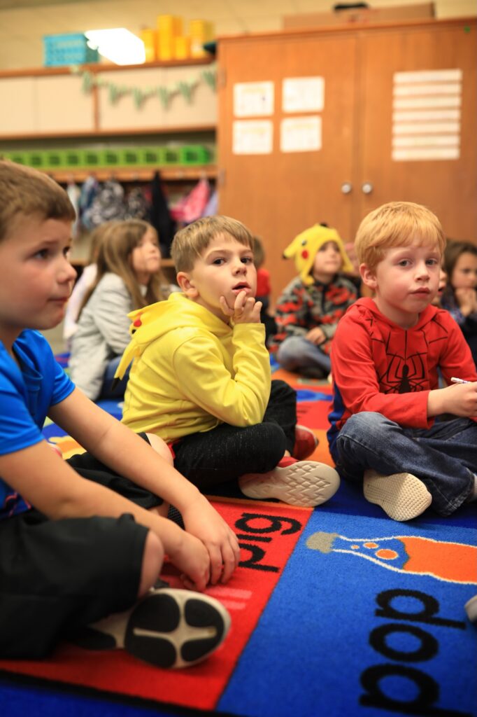 Children sitting on the floor in a classroom setting.