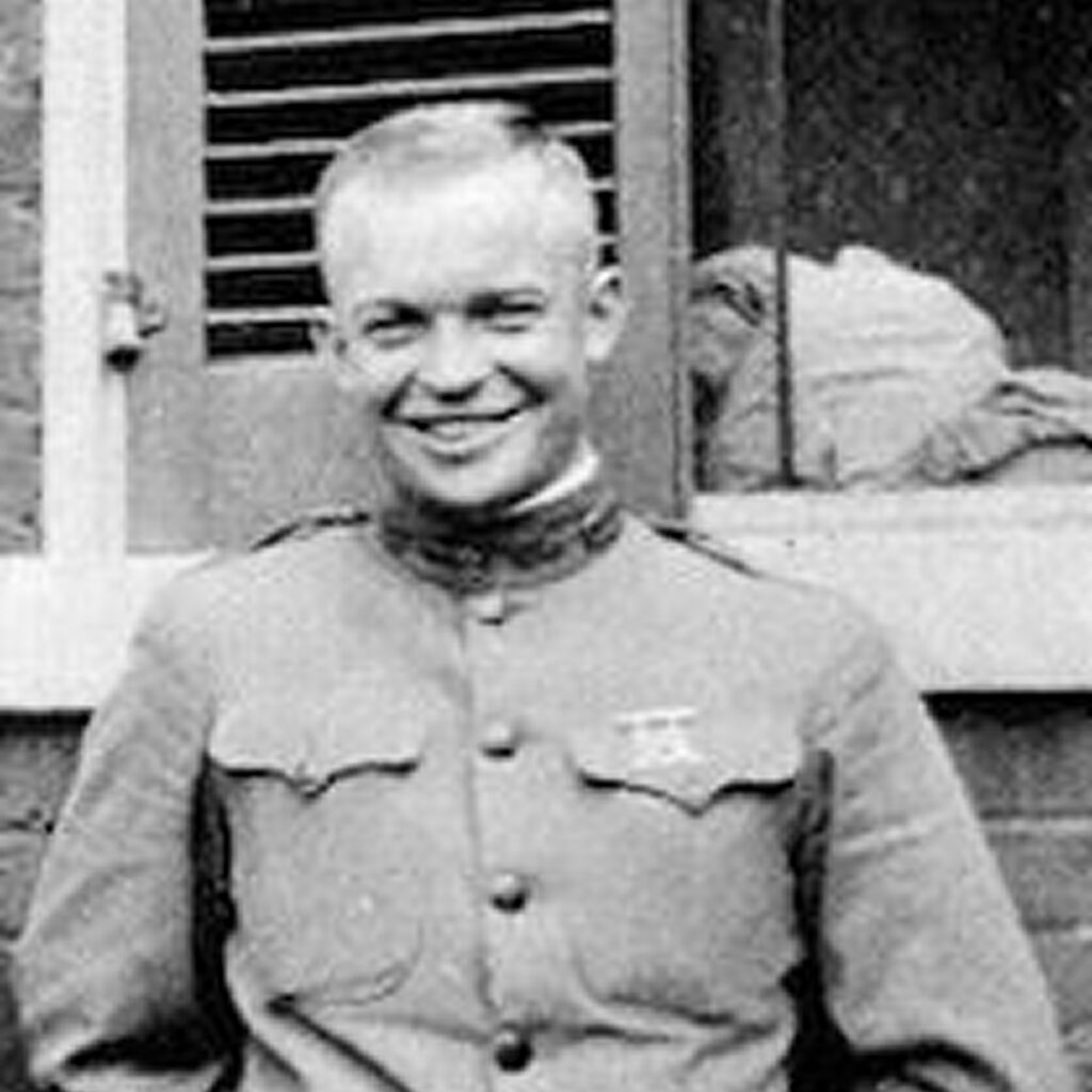Man in military uniform, standing and smiling, against a building with a window.