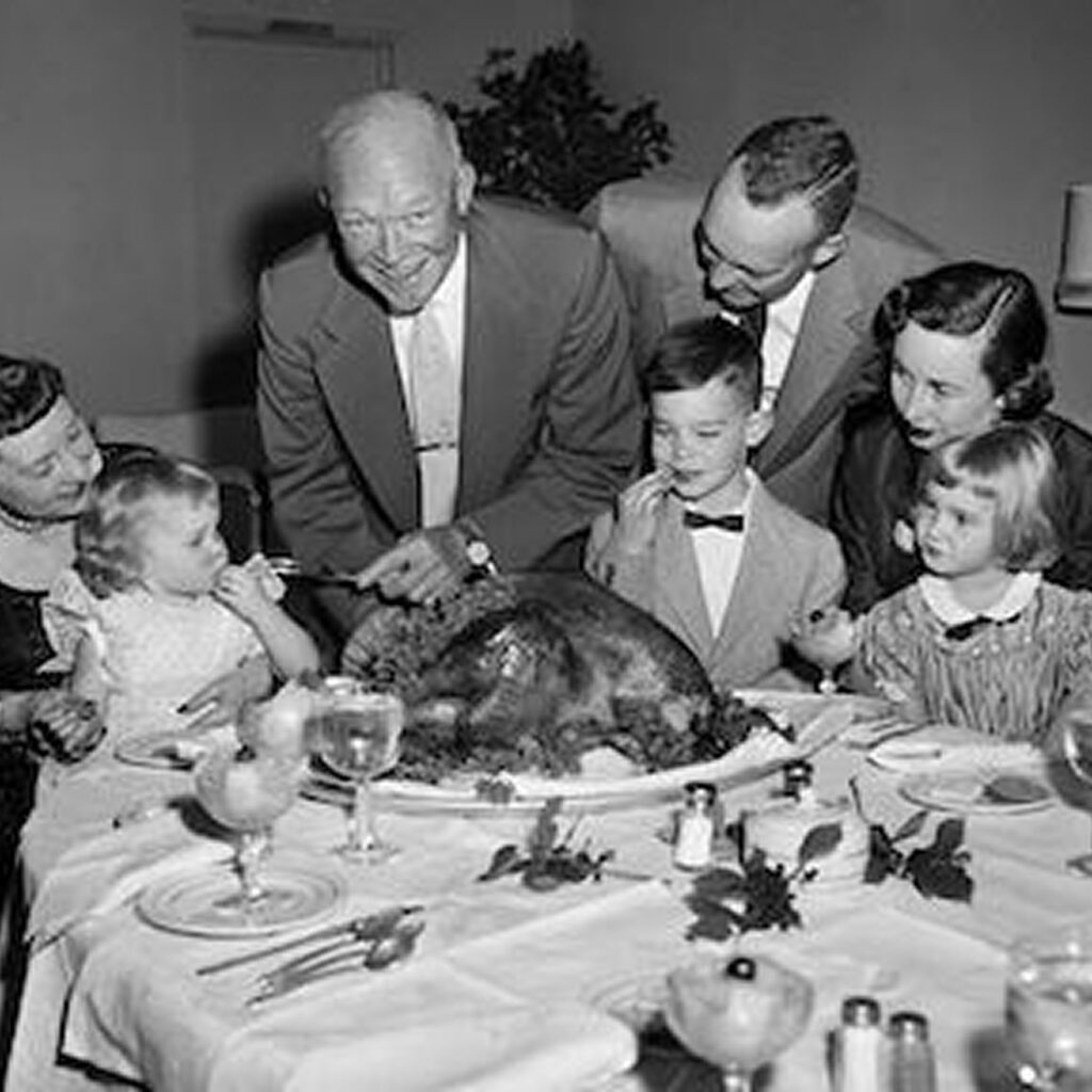 A group of people, including Dwight D. Eisenhower, gathered around a dining table, enjoying a holiday dinner with a turkey as the centerpiece.