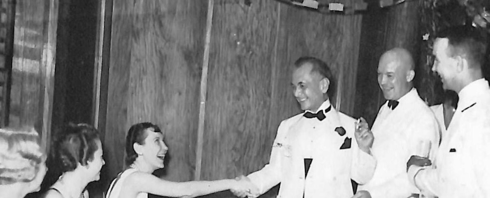 Cropped image of a young man in a white tuxedo shaking hands with a seated Mamie Eisenhower.