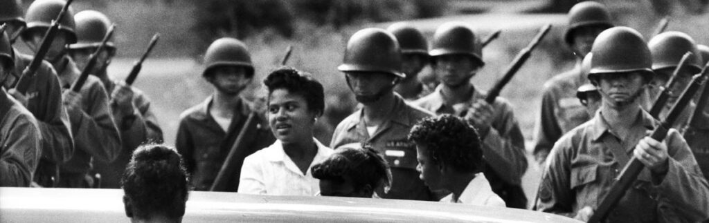 Black-and-white image of a man addressing a seated audience.