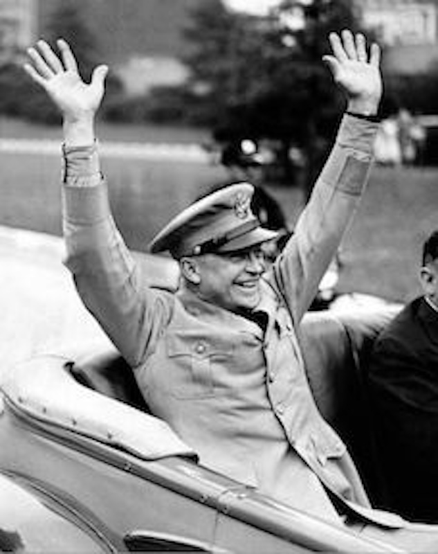 General Eisenhower in the back of a car, hands raised and smiling, on V.E. Day.