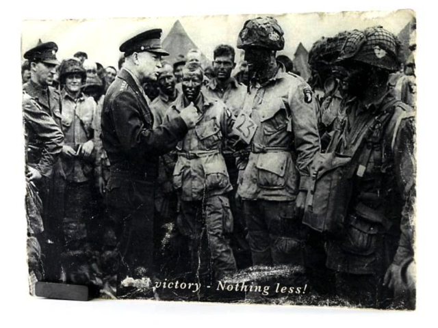 General Dwight D. Eisenhower speaking with a group of soldiers gathered outdoors, with overlayed text that reads "Victory - Nothing Less!"