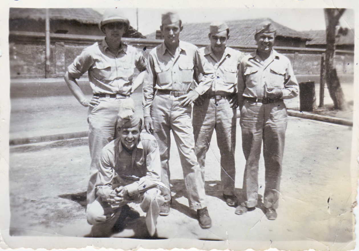 Group of sailors posing together outdoors in white naval uniforms.