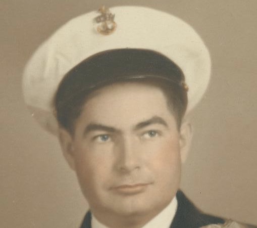 An older photograph in color featuring a male military officer in a dress uniform with a hat. He has a serious expression and is looking slightly to his right.
