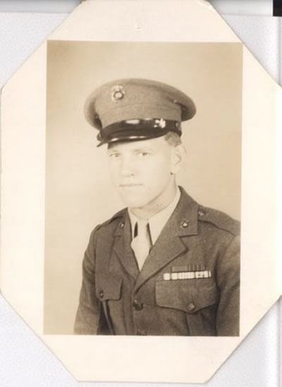 Serviceman wearing a dress military uniform and cap in a formal portrait.