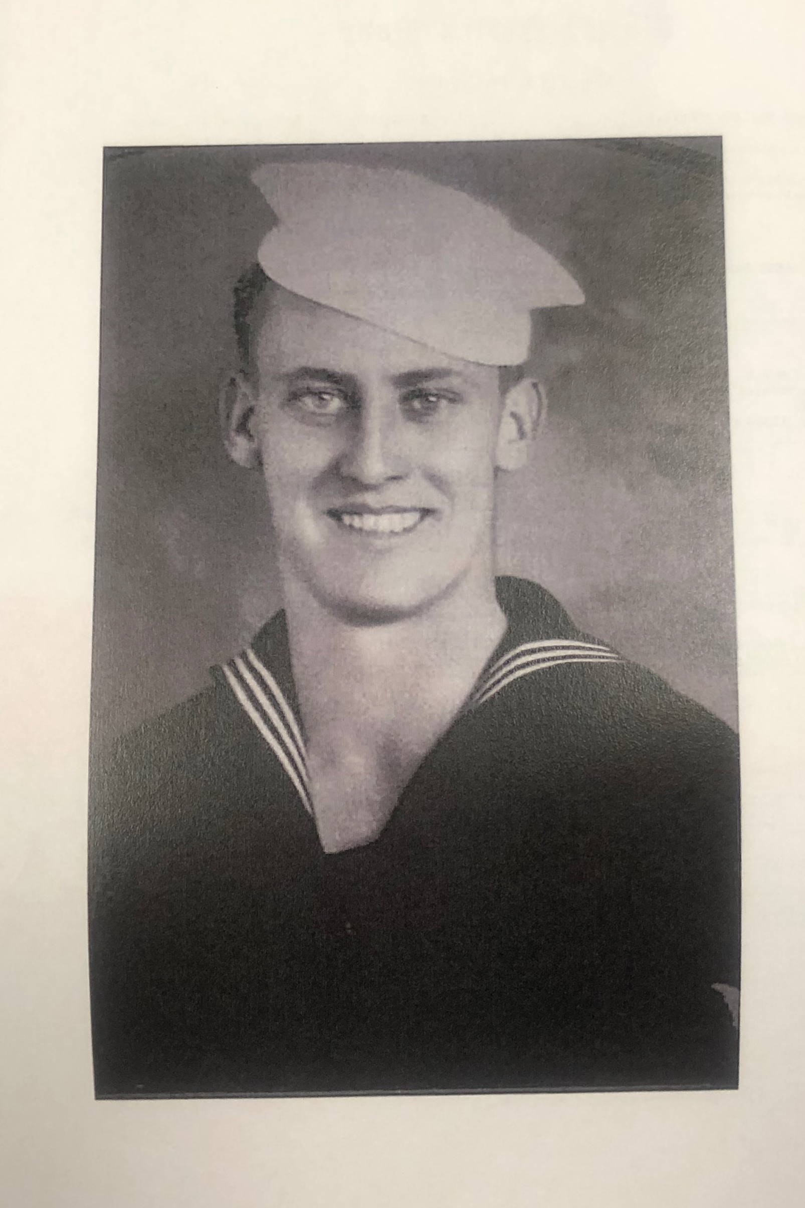 Smiling sailor wearing a dark U.S. Navy uniform and white cap.