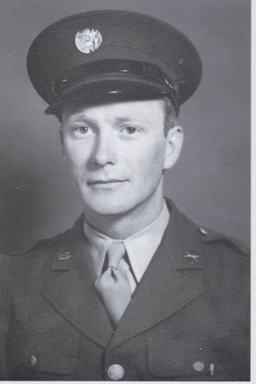 The image is of a man dressed in military attire, which includes a uniform, tie, and cap. He is looking directly at the camera with a slight smile.