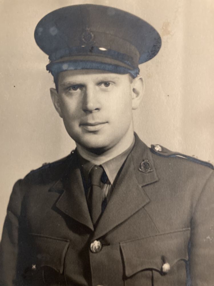 A black-and-white photograph of a man wearing a military uniform. He has short hair and is wearing a tie with a dark jacket.