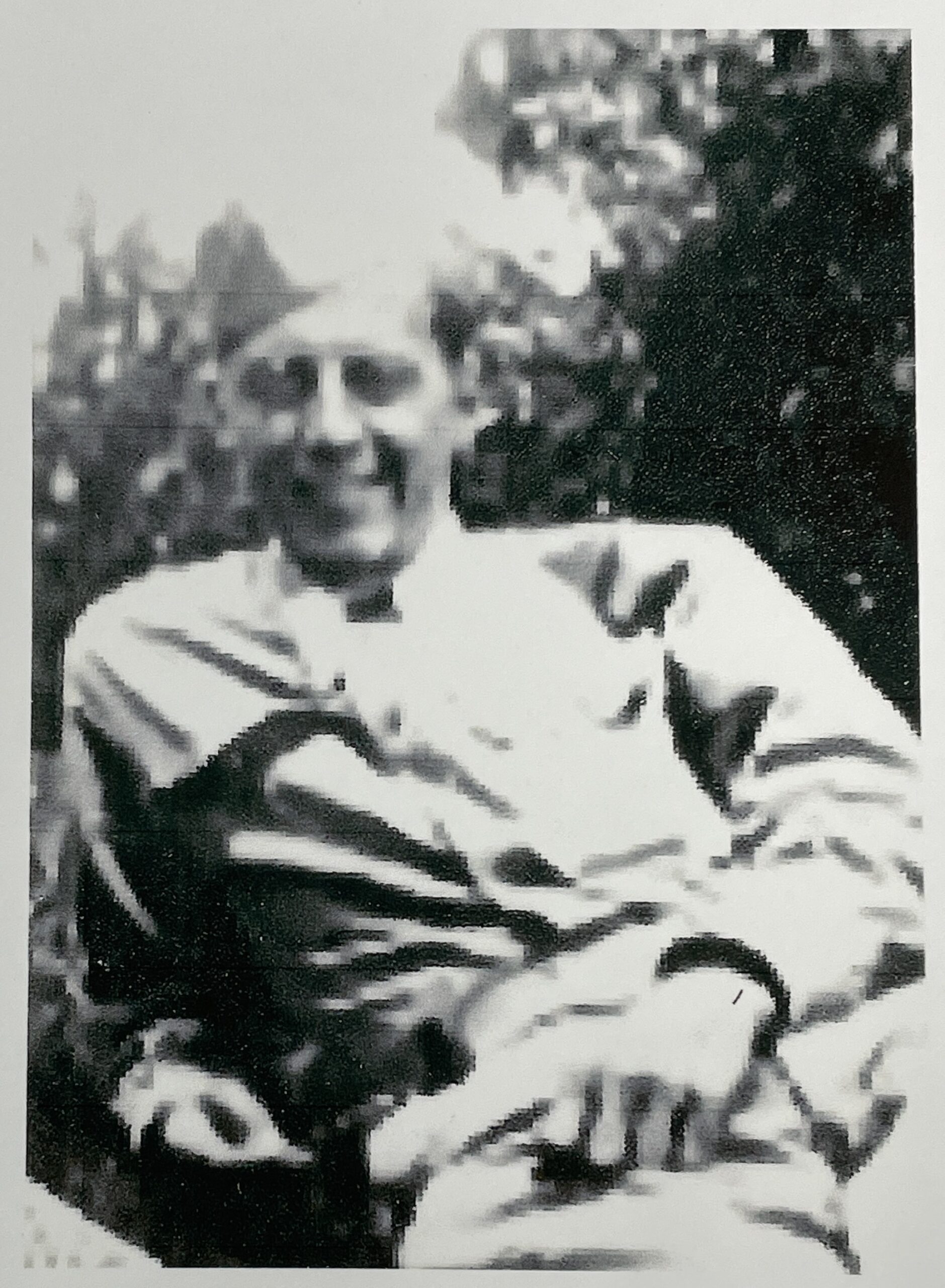 Smiling man seated outdoors in a light-colored shirt.