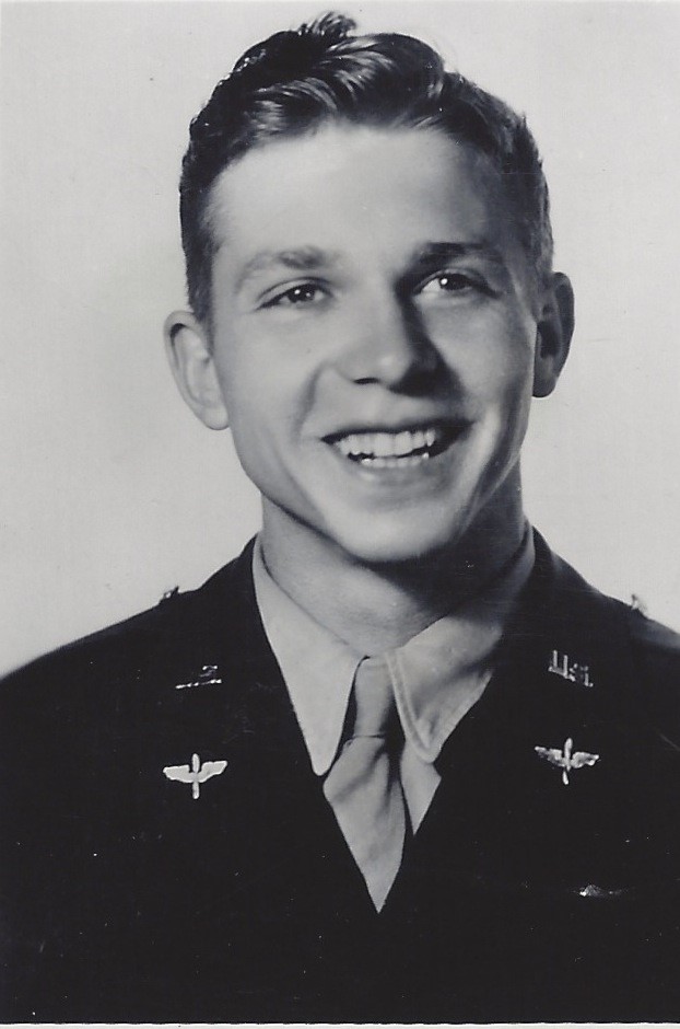 A black and white photo features a man wearing military attire, including an army uniform. His pose is relaxed, with a slight smile on his face. He is looking directly at the camera.