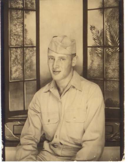 Young serviceman seated indoors in a light-colored military uniform.