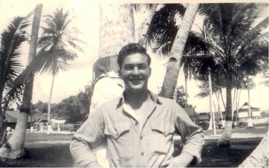Smiling serviceman outdoors beneath palm trees.