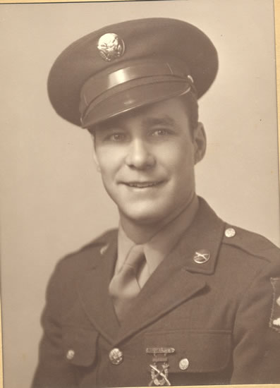 This is an old photograph of a man in military uniform. The man is smiling slightly and wearing a badge on his lapel.