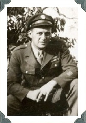 Serviceman seated outdoors in a military uniform and cap.