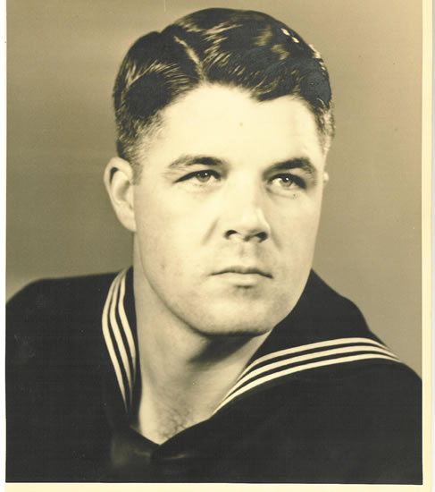 A sepia-toned black-and-white photograph of a man in a navy uniform with short hair and a stern expression.