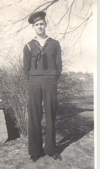 Sailor standing outdoors in a dark U.S. Navy uniform.