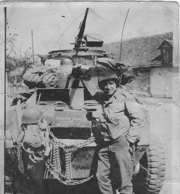 John Peter Bruszewski seated beside a military vehicle in uniform.