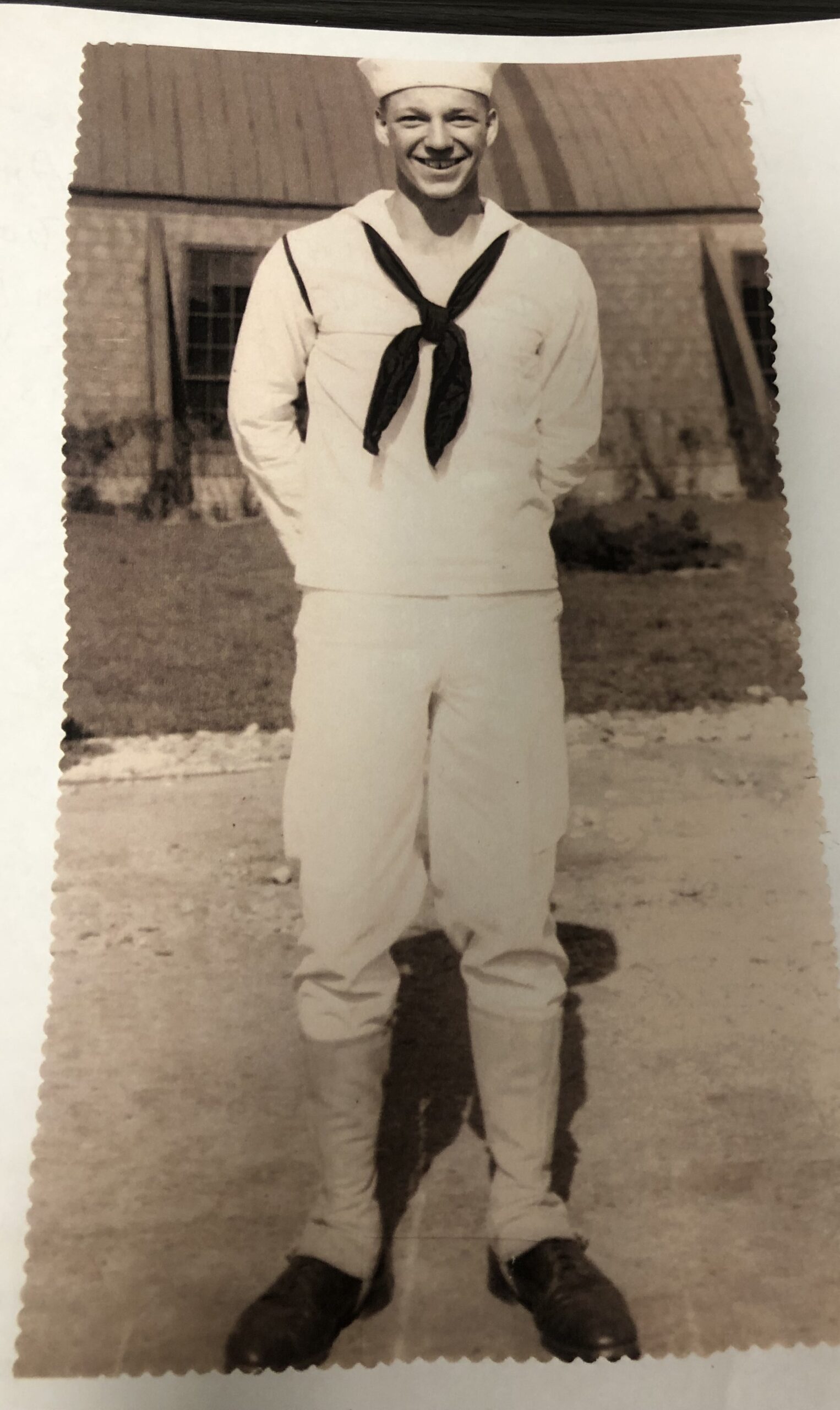 A young man dressed in a sailor uniform, possibly from the navy, posing with his hands behind him.