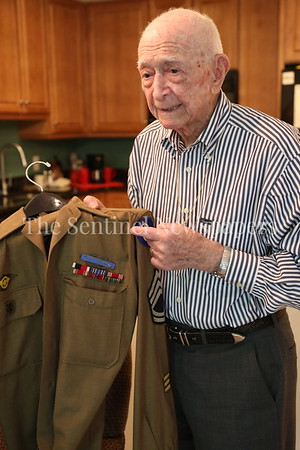 Elderly man examining a military jacket while standing indoors.