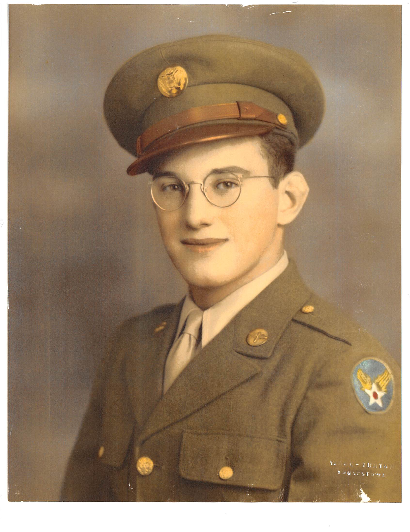 A man wearing a military uniform and glasses, is smiling at the camera.