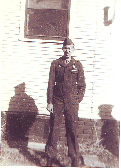 A man standing outside a building. He is wearing a military uniform and has a military-style haircut. The photo appears to be old and has a sepia tone, suggesting it might have been taken several decades ago.