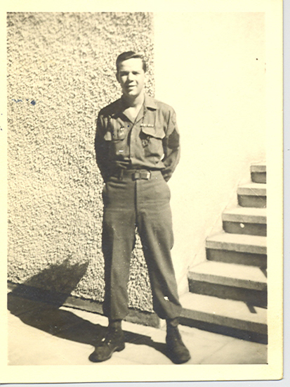 A man in military uniform standing against a wall.