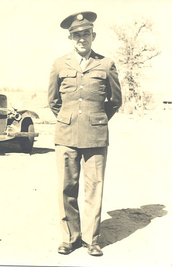 Black and white photograph of a man in military attire, standing outdoors.