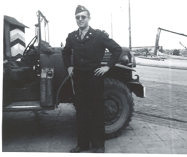 Serviceman standing beside a military jeep in uniform.
