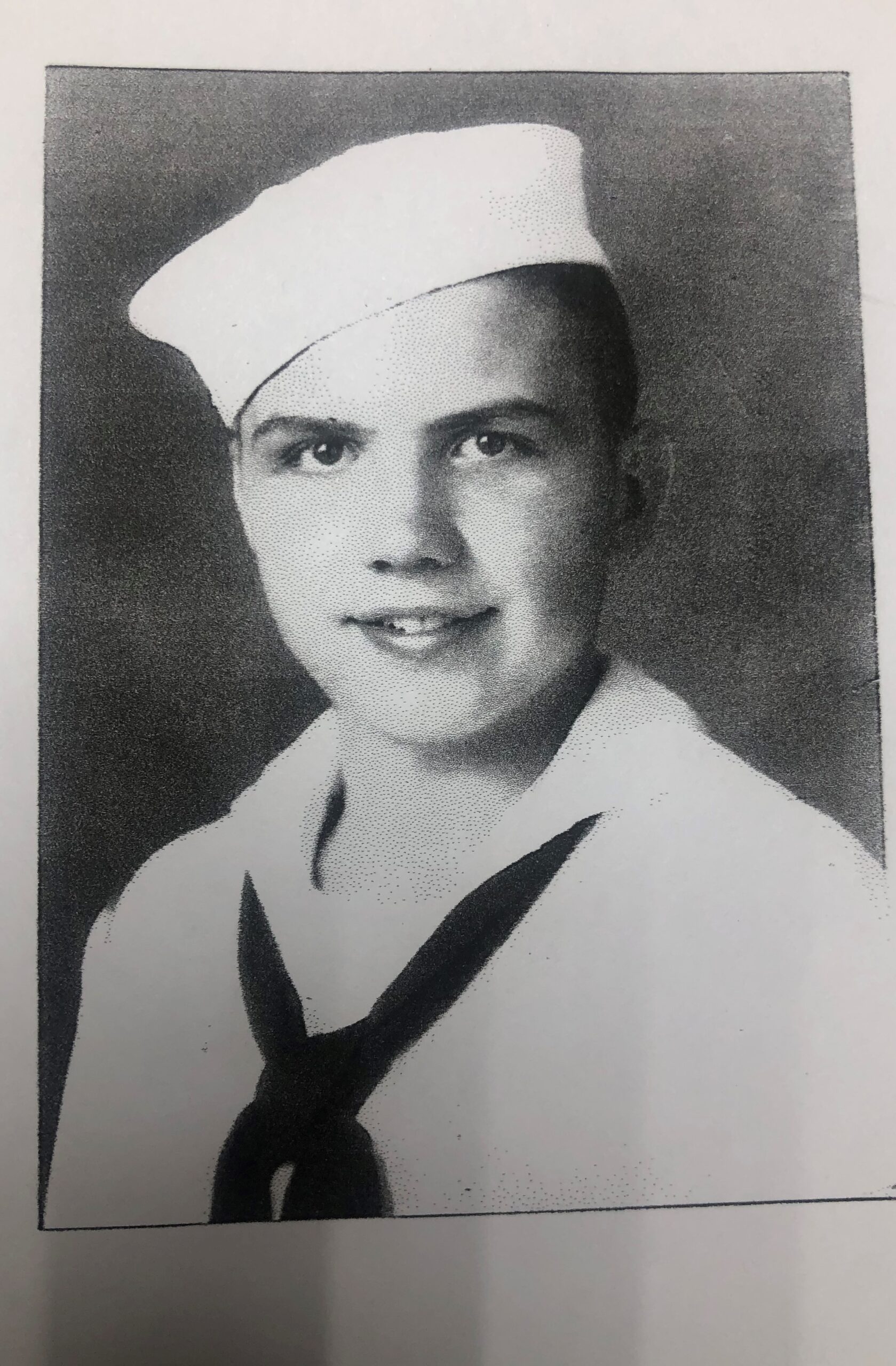 This is a black and white photo of a young male. He is wearing a sailor's uniform and has a tie around his neck. The individual appears to have short hair and is looking directly at the camera.