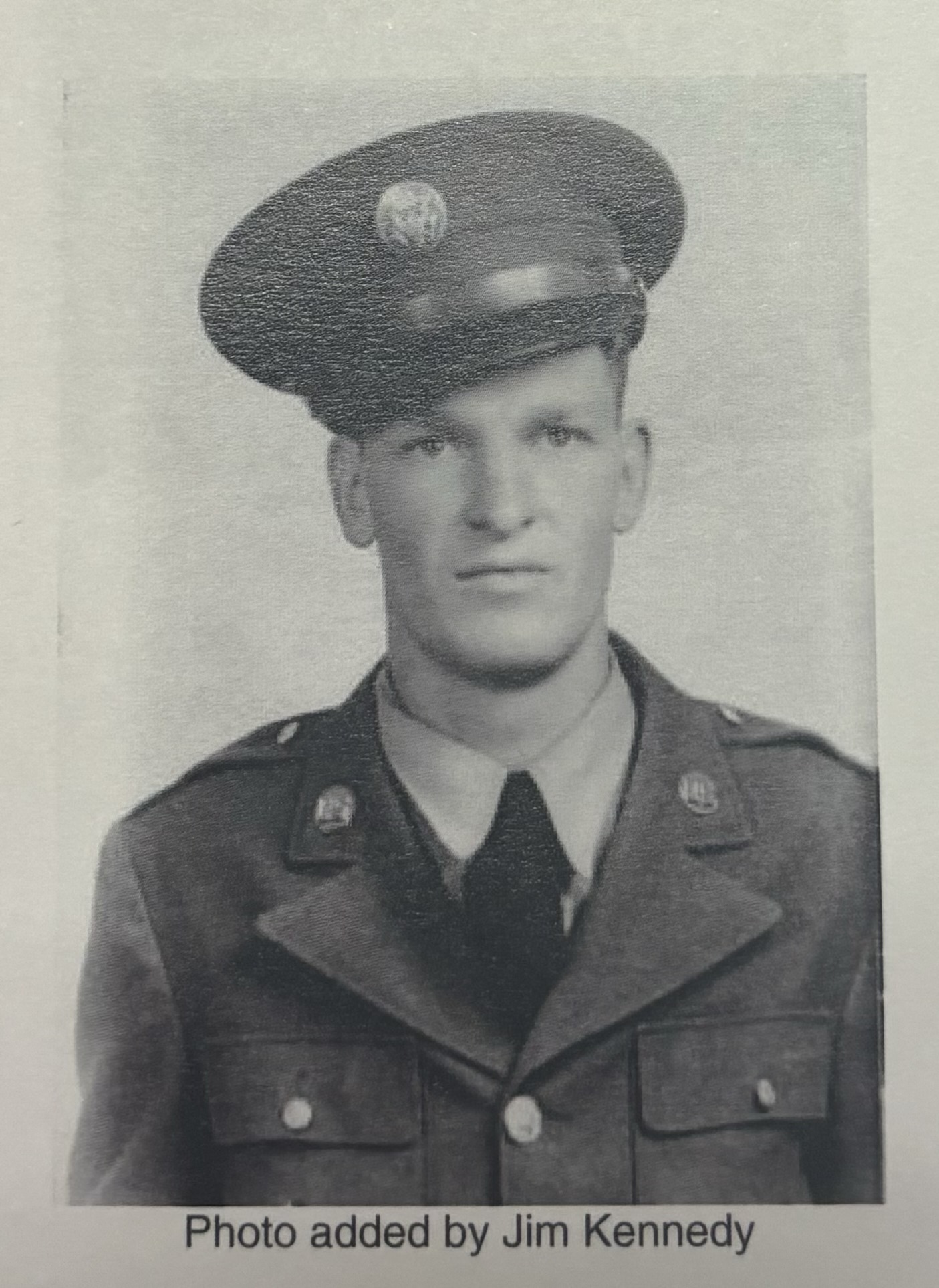 A man wearing a military uniform and a cap. He is looking at the camera with a somber expression.