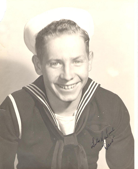 A young man in a sailor's uniform smiling at the camera.