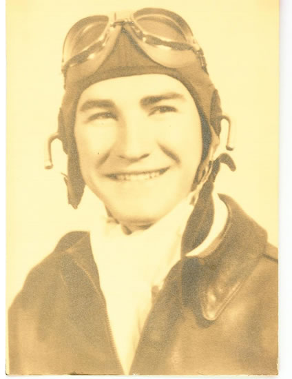 A black and white photograph featuring an individual who appears to be a pilot, smiling at the camera, adorned with aviator goggles and donning a military uniform.