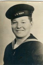 The image displays an old black-and-white photograph of a man who appears to be in his late 20s or early 30s. He is wearing a navy sailor's uniform. He is smiling at the camera.