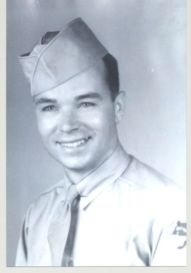 A military man in uniform, smiling and looking directly at the camera. He has a cap on his head.