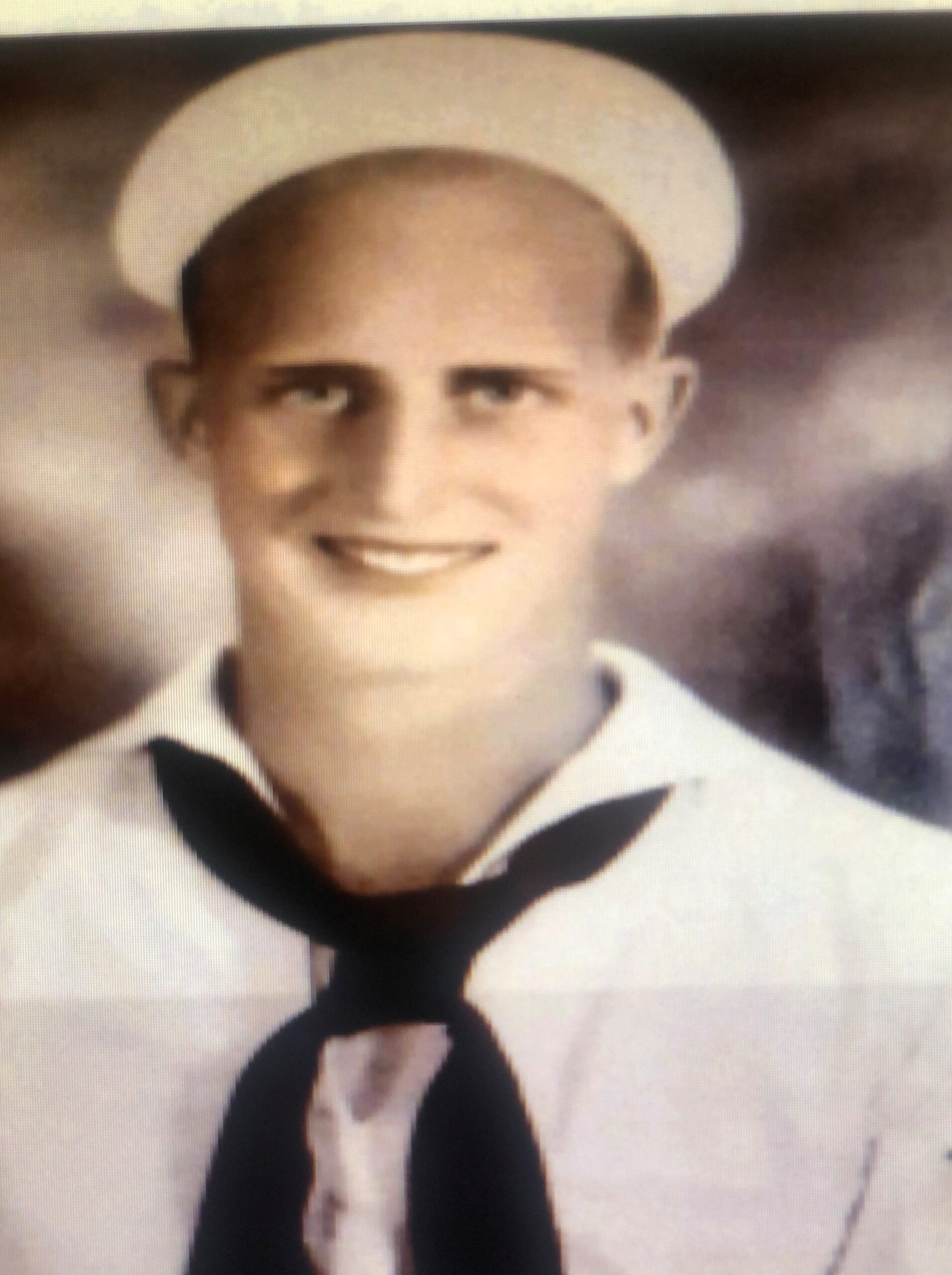 Smiling sailor wearing a white U.S. Navy cap.