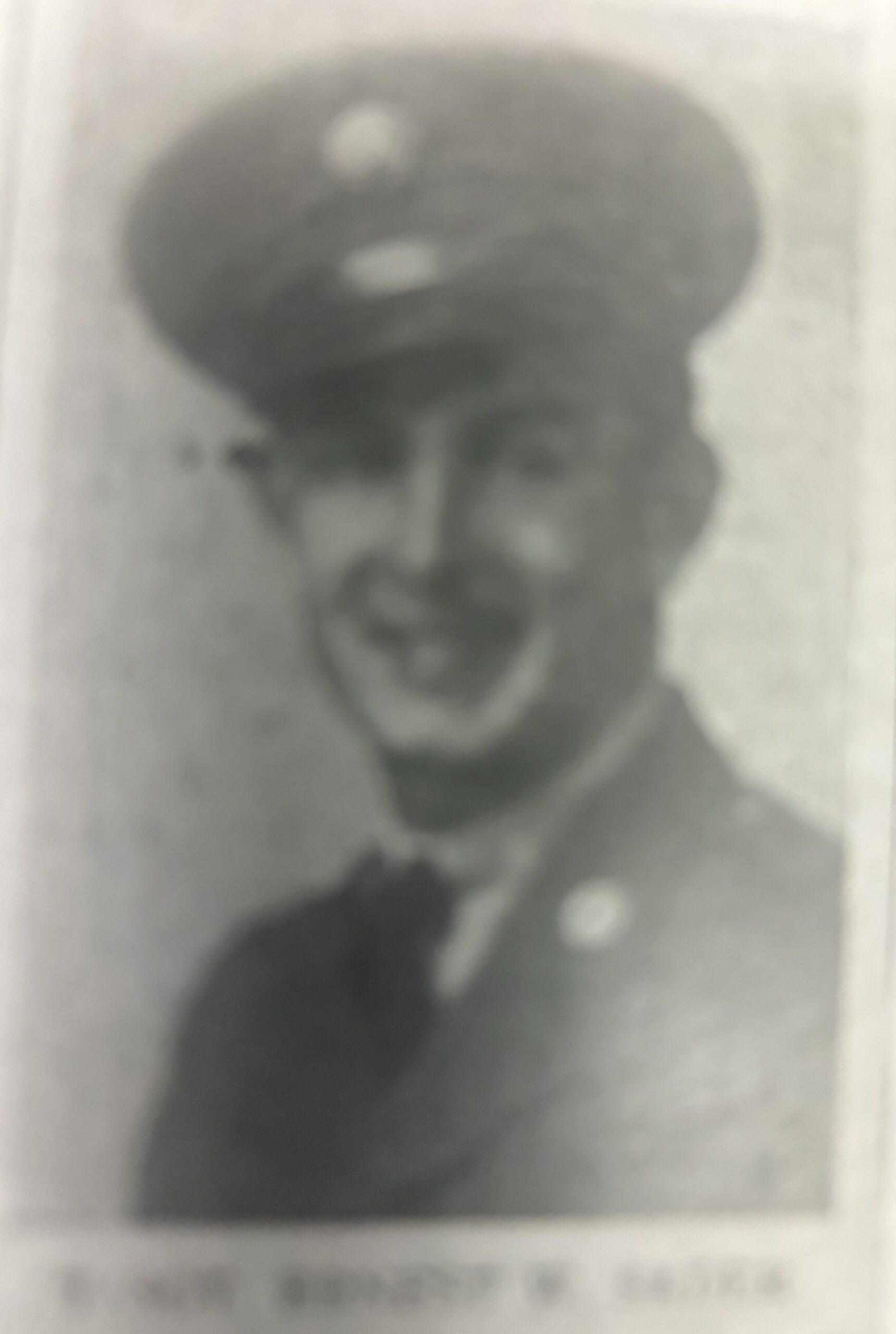 Smiling serviceman wearing a military uniform and cap in a faded portrait.